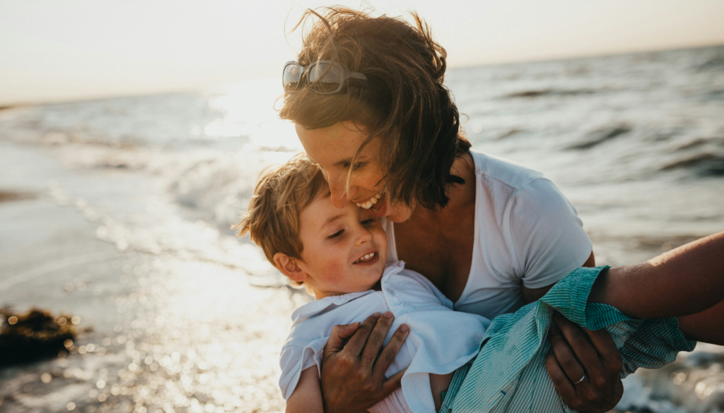 mom holding son, both laughing, at a st. simons beach