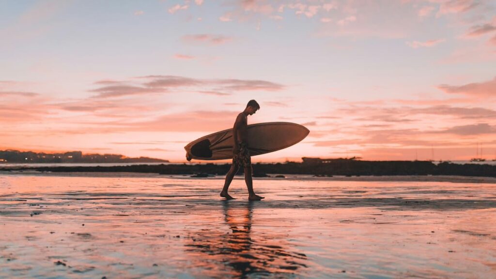 Boy carrying a surfboard on the beach while on a family vacation in Tamarindo