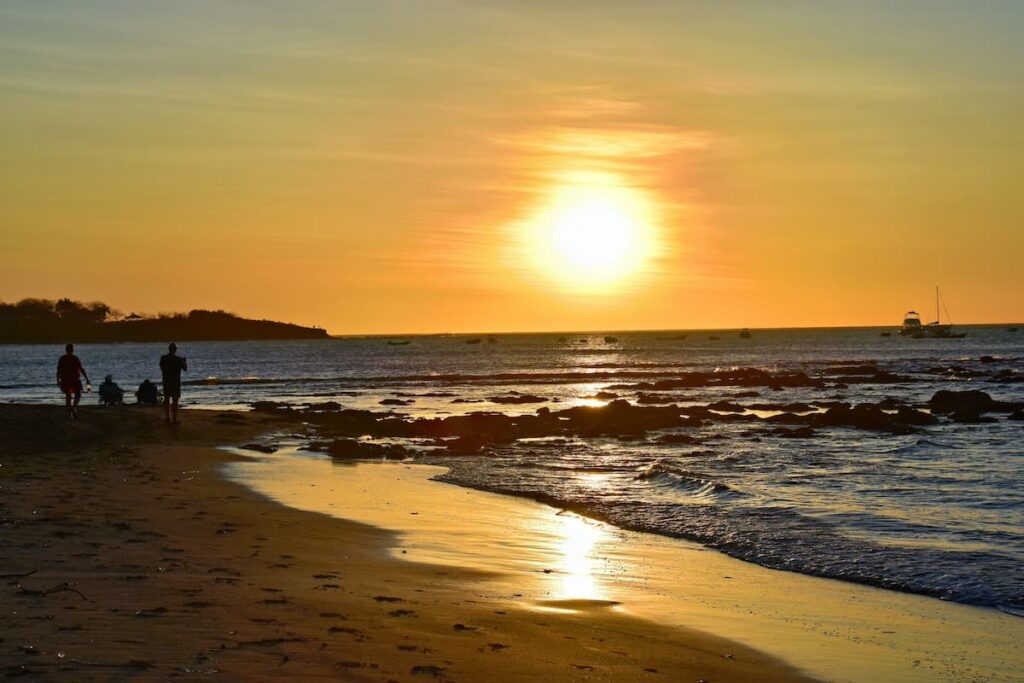 People watching the sunset at Tamarindo beach with boats in the water in the background