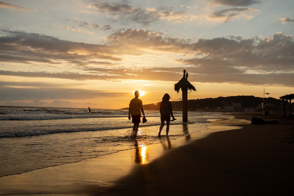 Couple walking barefoot on beach sunset while on their honeymoon