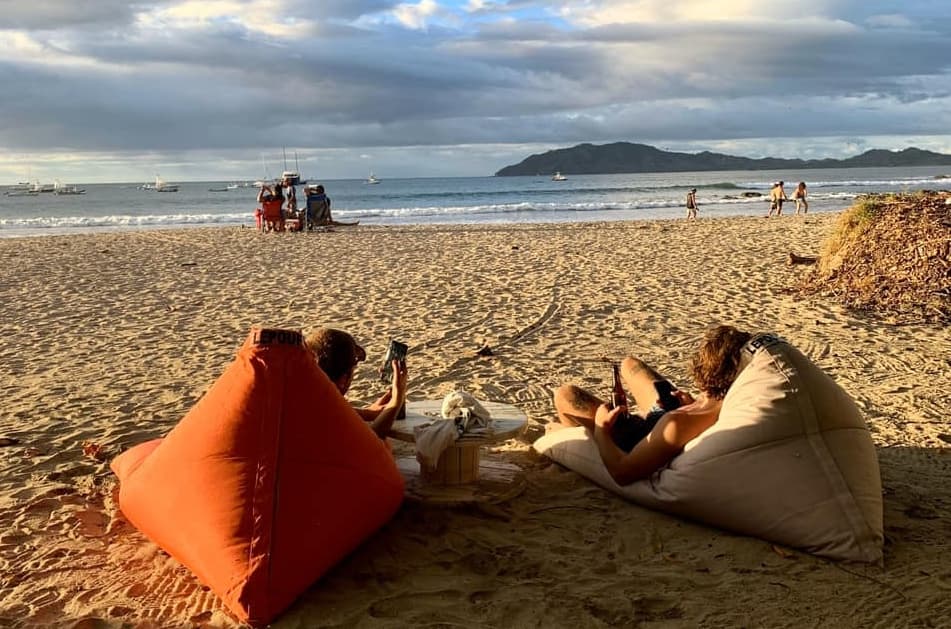 Two men sitting on beanbags on the sand and sipping beer waiting for the sunset in Tamarindo Costa Rica outside the El Chiringuito beach bar