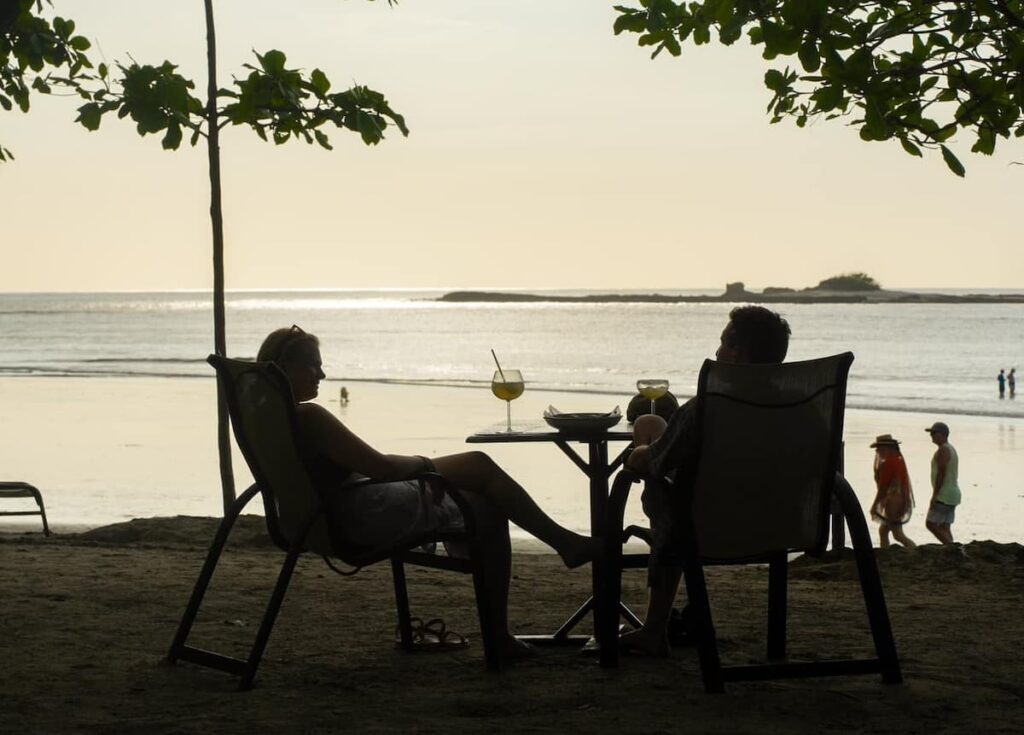 A couple sitting at Langosta Beach Club in tamarindo sipping cocktails in front of ocean views