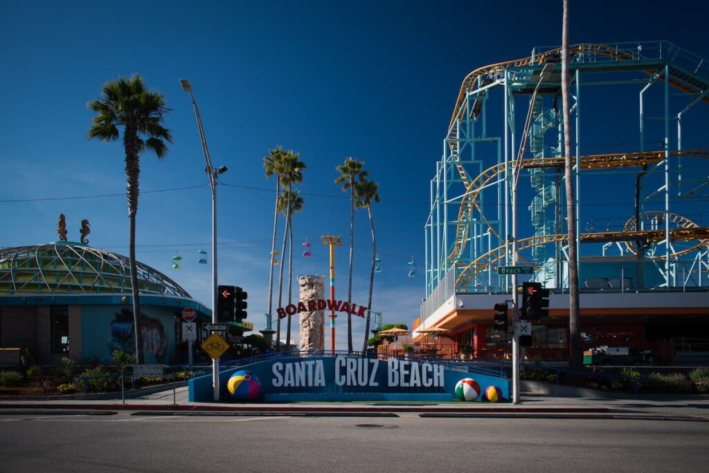 Santa Cruz Beach sign with palm trees and rollercoaster in background
