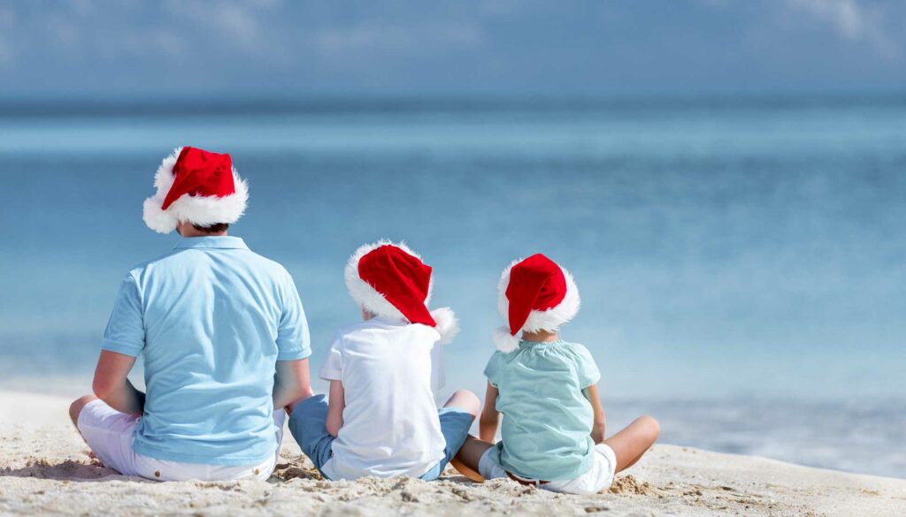 a man and two sons wearing santa caps at the beach