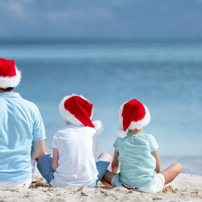 a man and two sons wearing santa caps at the beach