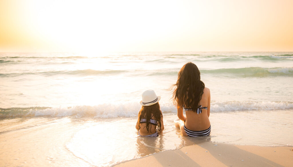 mom and daughter sitting on the beach watching the sunset