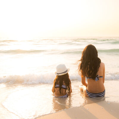 mom and daughter sitting on the beach watching the sunset