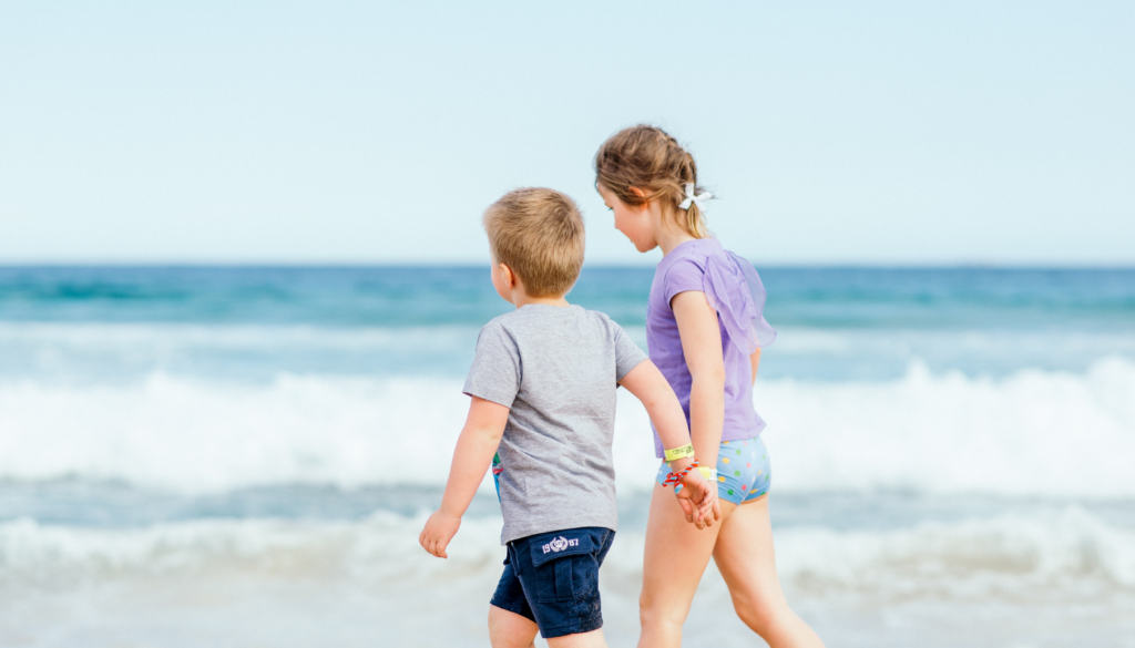brother and sister holding hands and walking on the beach