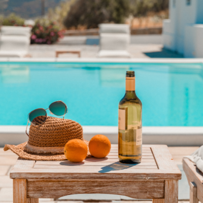 beach hat, bottle of wine, and sunglasses on table overlooking a pool