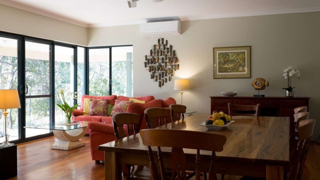 Vaila's living area with large wooden dining table with an L-shaped red couch
