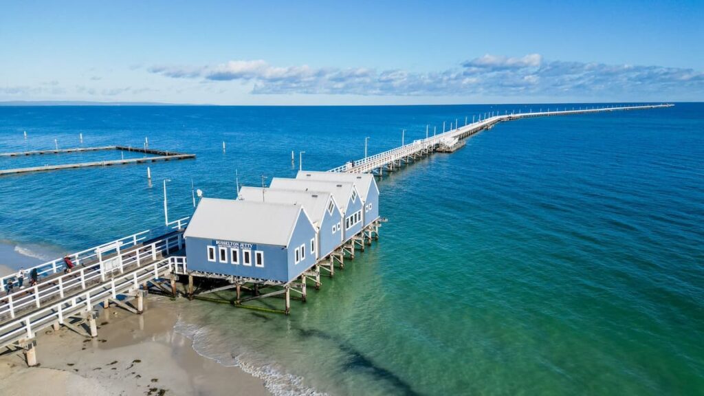 Aerial view of Busselton jetty with clear blue waters surrounding it and a light blue cabin at the start of the jetty