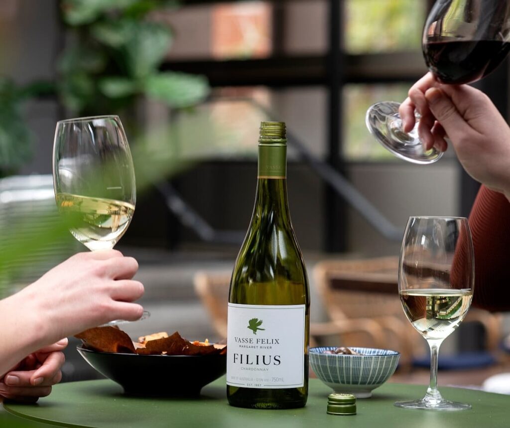 Three wine glasses and a bottle of white wine with two bowls on a green table at the Vasse Felix Winery