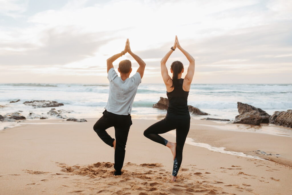 couple doing yoga on a beach in dunbsborough