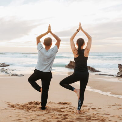 couple doing yoga on a beach in dunbsborough