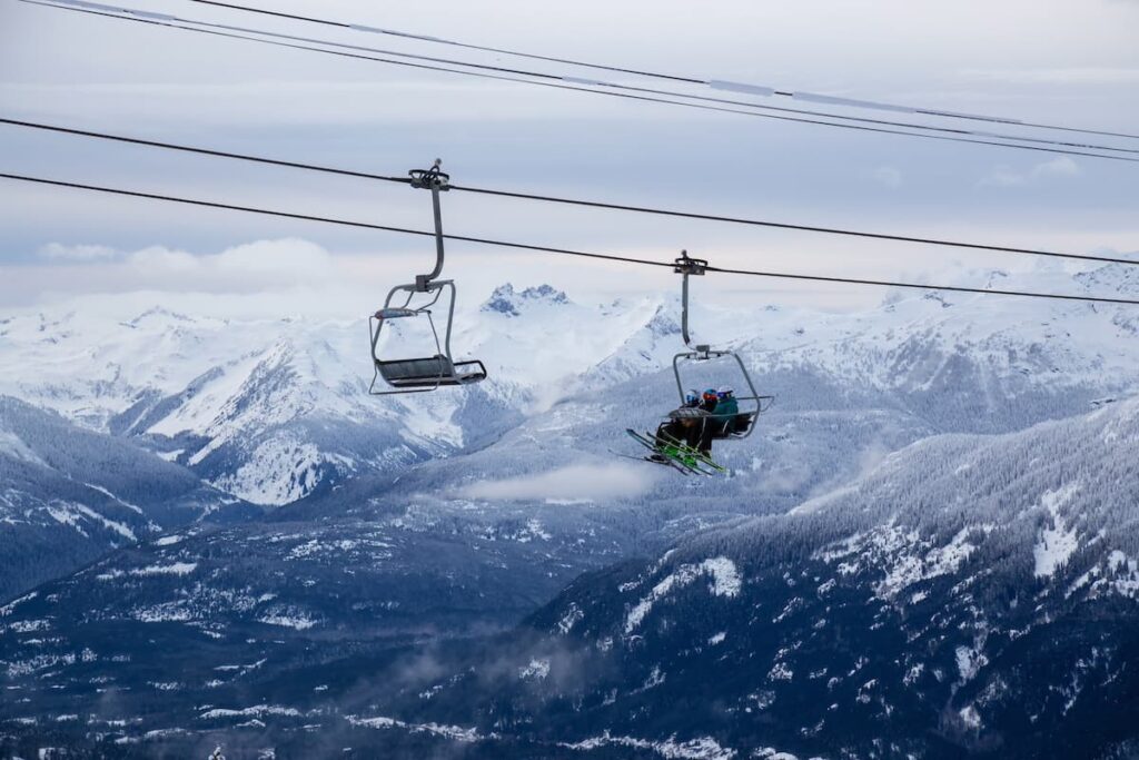 Skiiers on Whistler chair lift with snow-covered mountains in the background.