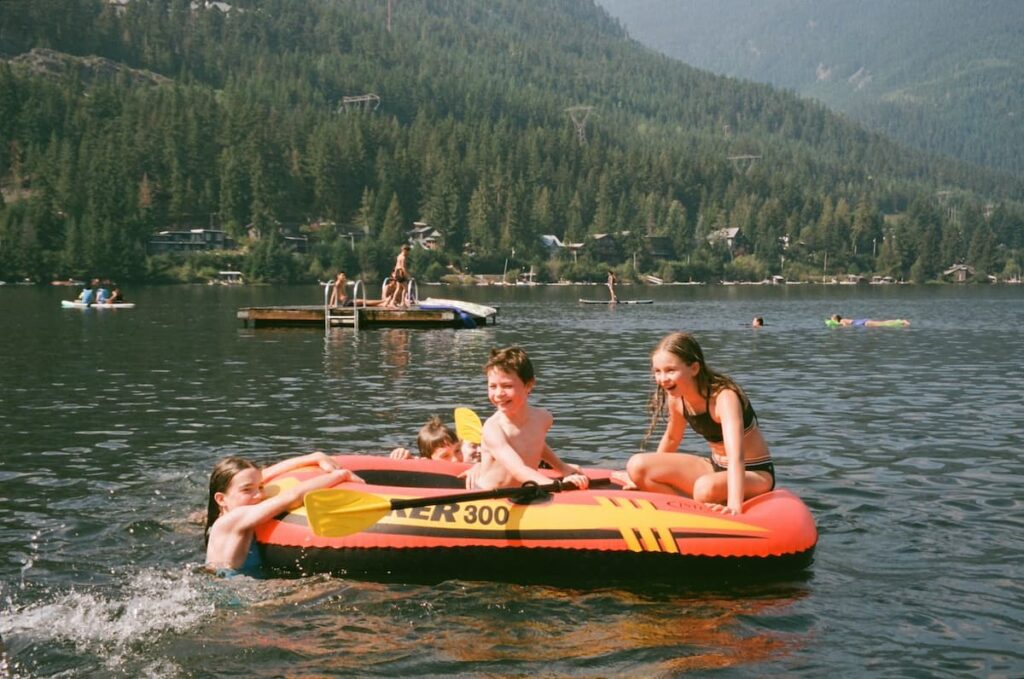 Kids playing on inflatable boat on a sunny summers day at a lake in Whistler with green trees in background