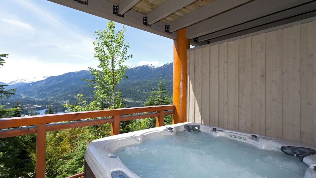Private hot tub on decking with mountain and lake views in background on a sunny day