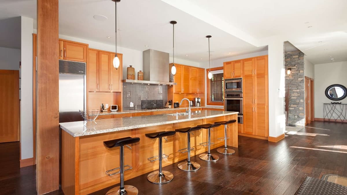 Large kitchen with wood furnishings and a long kitchen island with five black stools tucked into it