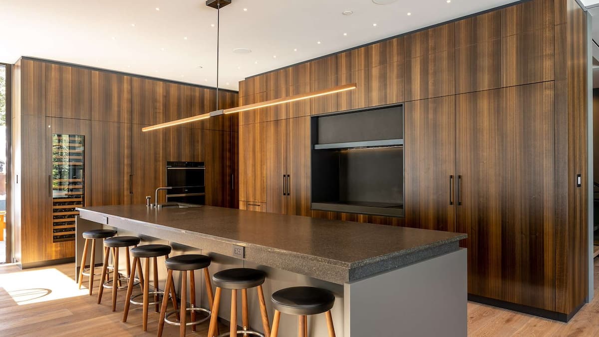 Large open plan kitchen with dark wood features and large kitchen island with 6 stools tucked underneath it