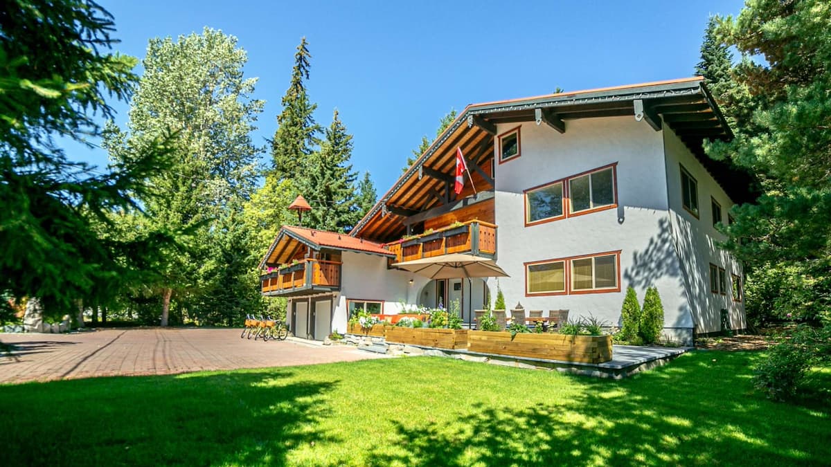 Exterior of Chalet Whistler surrounded by green cut grass and tall green trees on a sunny day with blue skies