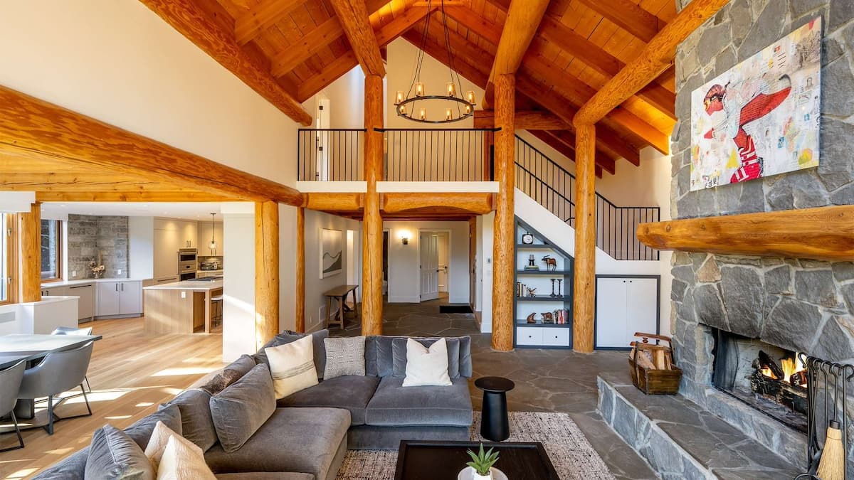 Large living space with tall vaulted ceilings and wooden beams and a floor to ceiling stone fireplace with a large grey L shaped couch