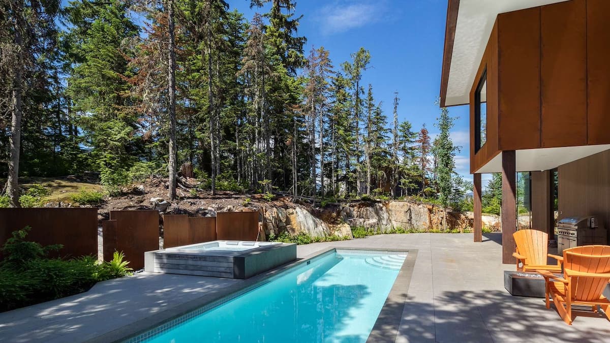 Outdoor area for Winterfell Whistler Chalet with orange patio furniture and a full length pool and hot tub surrounded by tall green trees