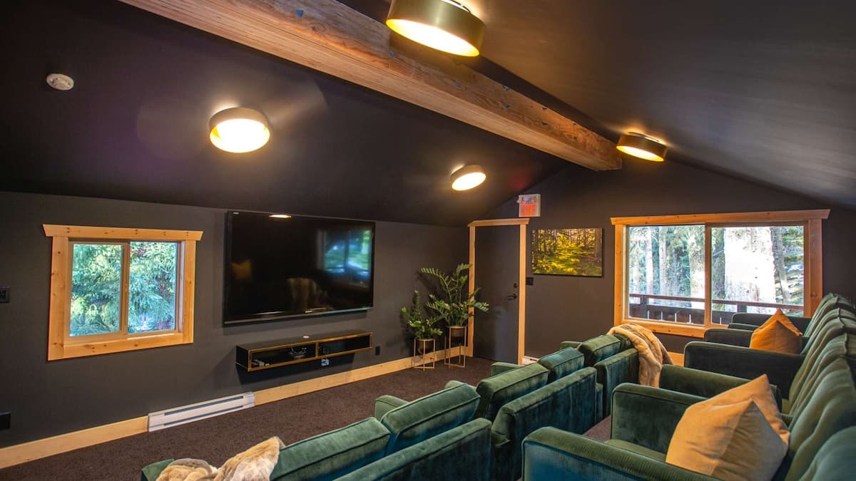 Media room with multiple green armchairs and dark black walls and a large wood beam running across the ceiling
