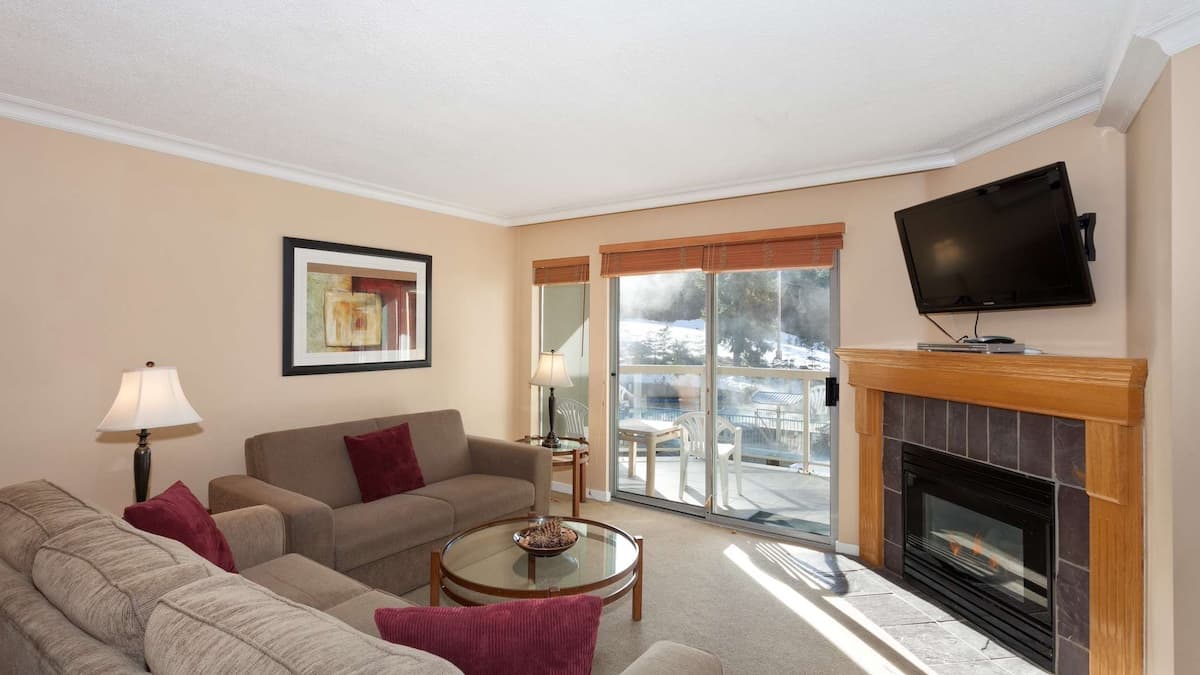 Cozy living area with two brown couches and fireplaces with tv over it and sliding doors out to private balcony