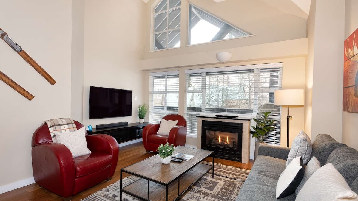 Tall ceiling living room with grey couch and two red leather arm chairs with brown coffee table and fireplace