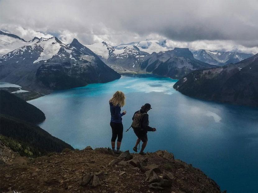 A man and a woman hiking on mountain with blue Garibaldi Lake