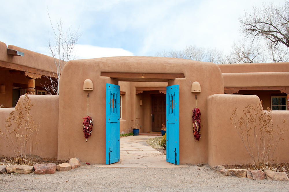 pueblo style home in Santa Fe, NM with bright blue double doors open wide