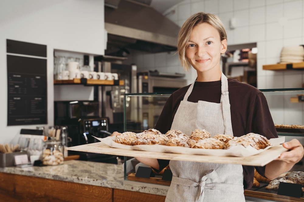 woman in bakery holding pan of baked goods