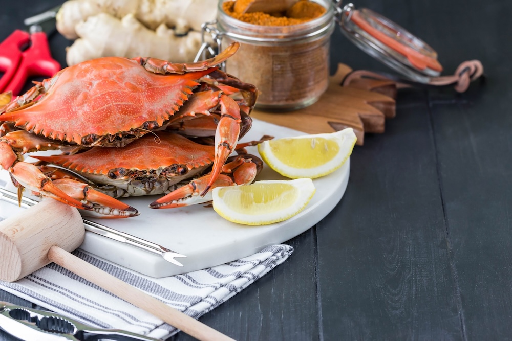 two Dungeness crabs on a plate with lemons, herbs and crab cracking tools