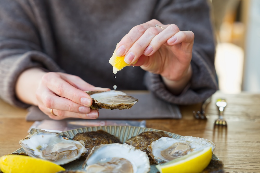 woman squeezing lemon on a half-shell oyster.