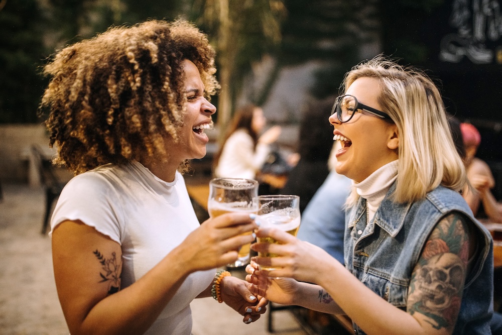 two women outside at a brewery, each holding a glass of beer