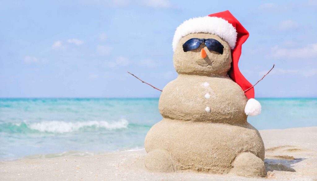 snowman wearing a santa cap and sunglasses made out of sand at the beach