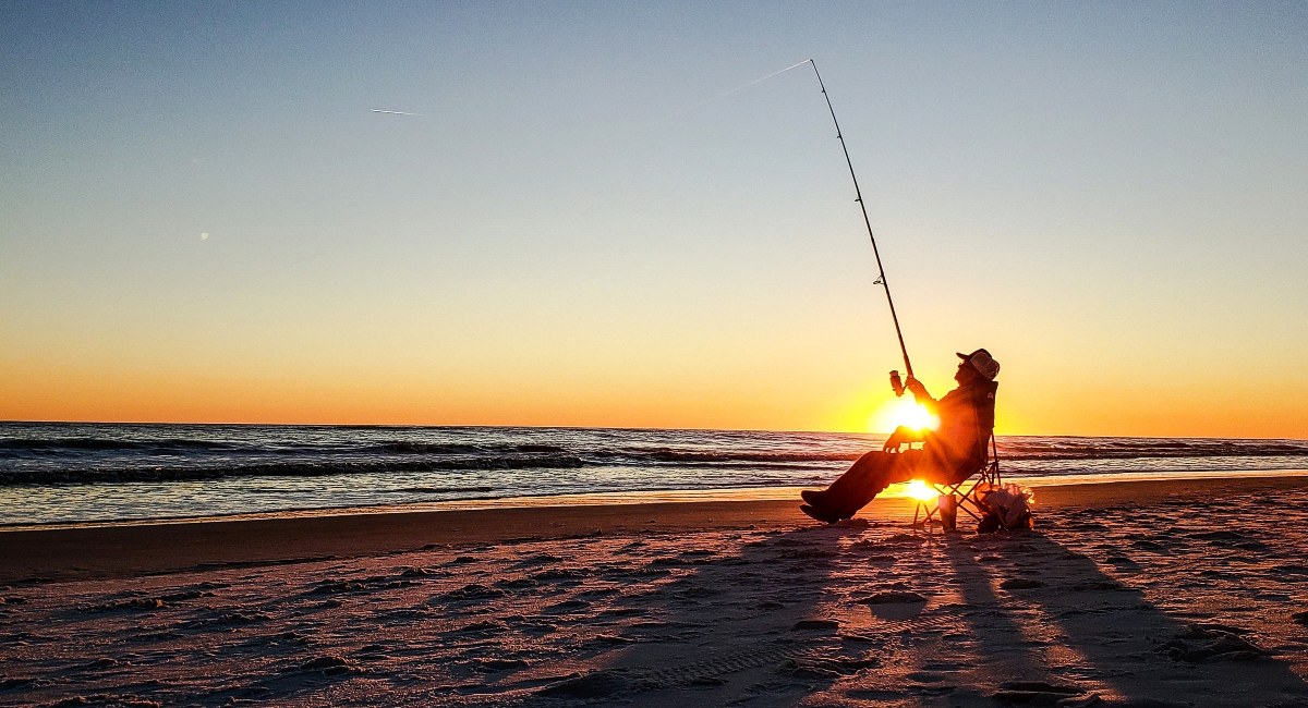 Active senior surf fishing in Destin at the beach during golden hour as the sun goes down