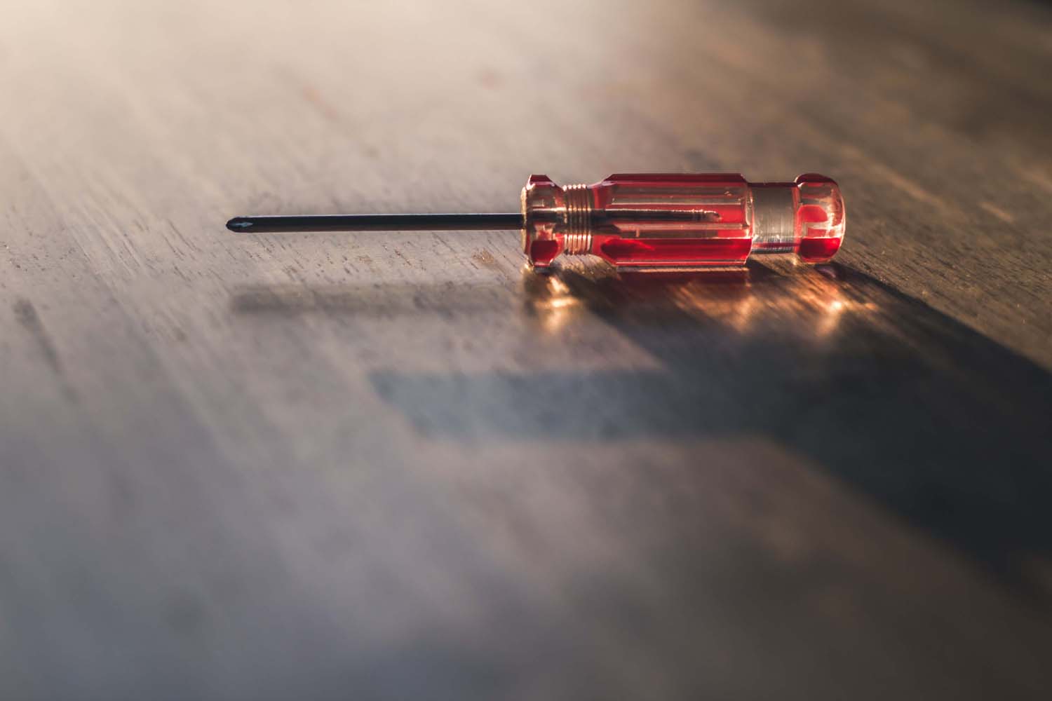 A close-up of a red-handled Phillips head screwdriver resting on a wooden surface, highlighting the importance of reliable tools in property repairs and maintenance.