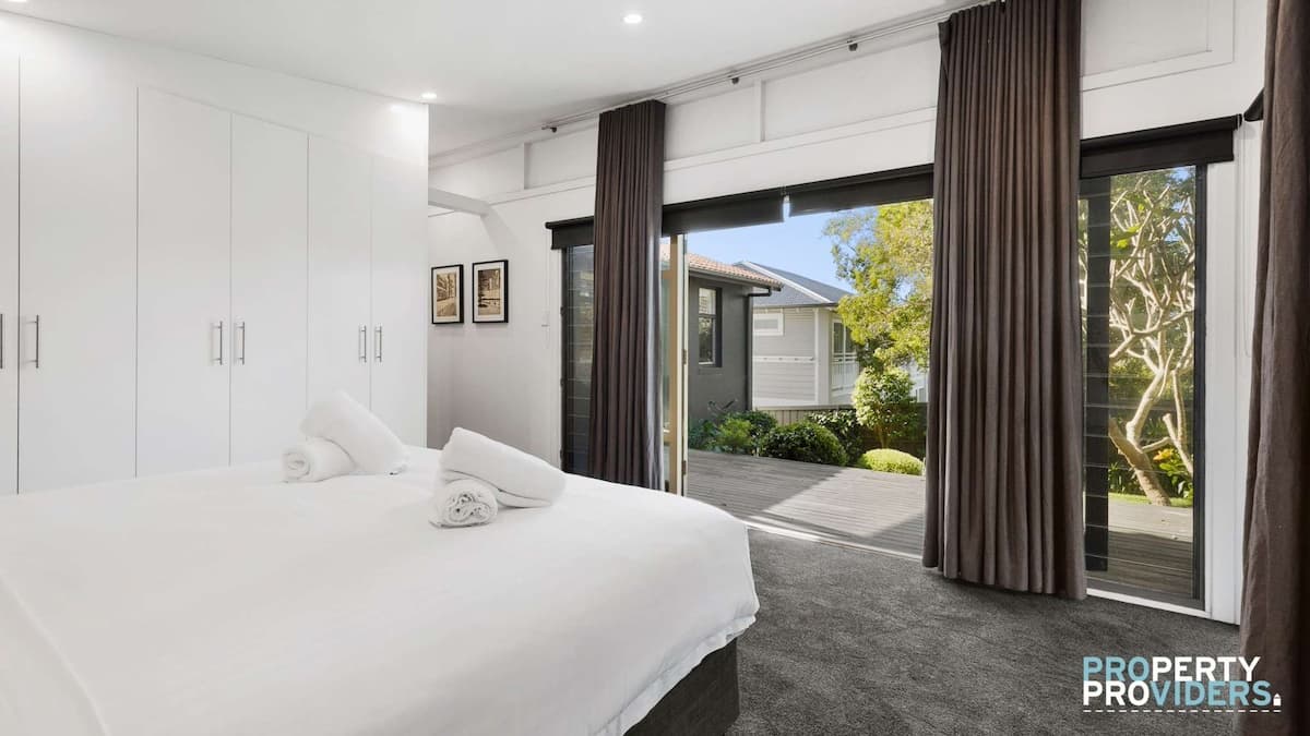 Master bedroom with white linens, white towels and white wardrobes. Large open doors out to private patio