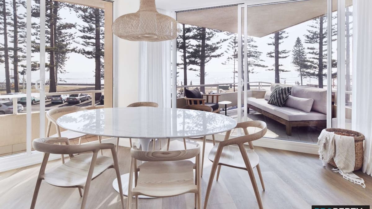 Round 6 person dining table with wooden seats next to floor to ceiling sliding doors out to spacious balcony overlooking the ocean