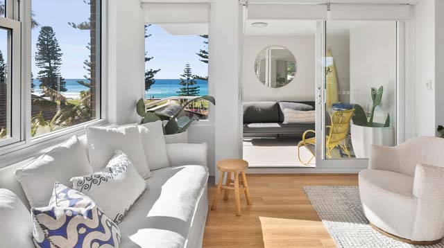 Modern living room opening to a balcony with a sea view, featuring a white sofa, armchairs, and minimalist decor in Manly, Sydney.