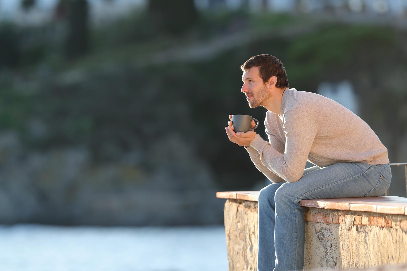 Man enjoying a serene morning with a cup of coffee, overlooking a scenic landscape from a coastal rental property.