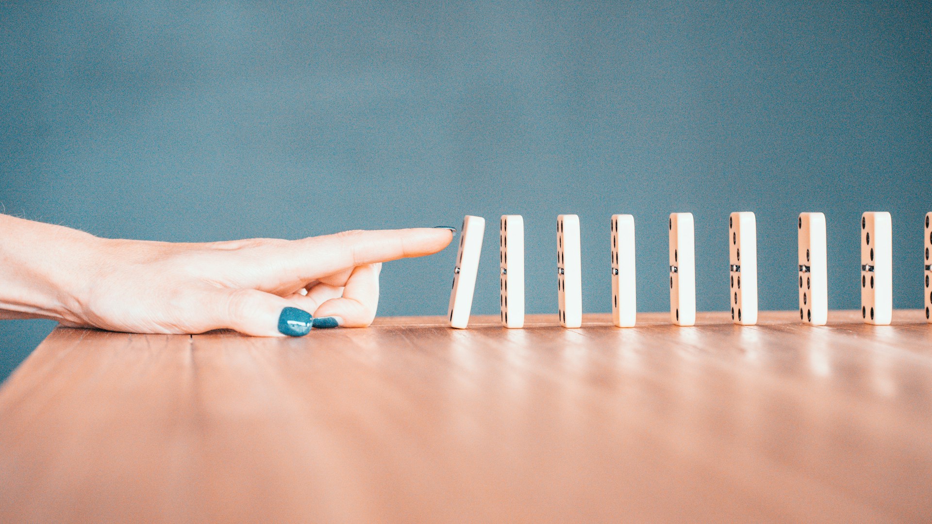 Finger pushing the first in a line of dominoes, symbolizing the cascading effect of rejecting short-term rental bookings on search rankings.