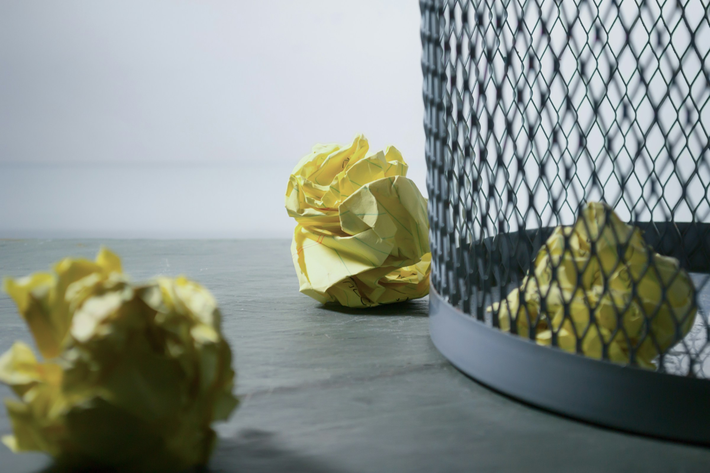 Crumpled yellow paper balls beside a mesh trash bin, symbolizing discarded ideas or rejected rental bookings.