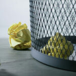 Crumpled yellow papers beside a trash can, symbolizing the discarded opportunities and consequences of cancelling short-term rental bookings.