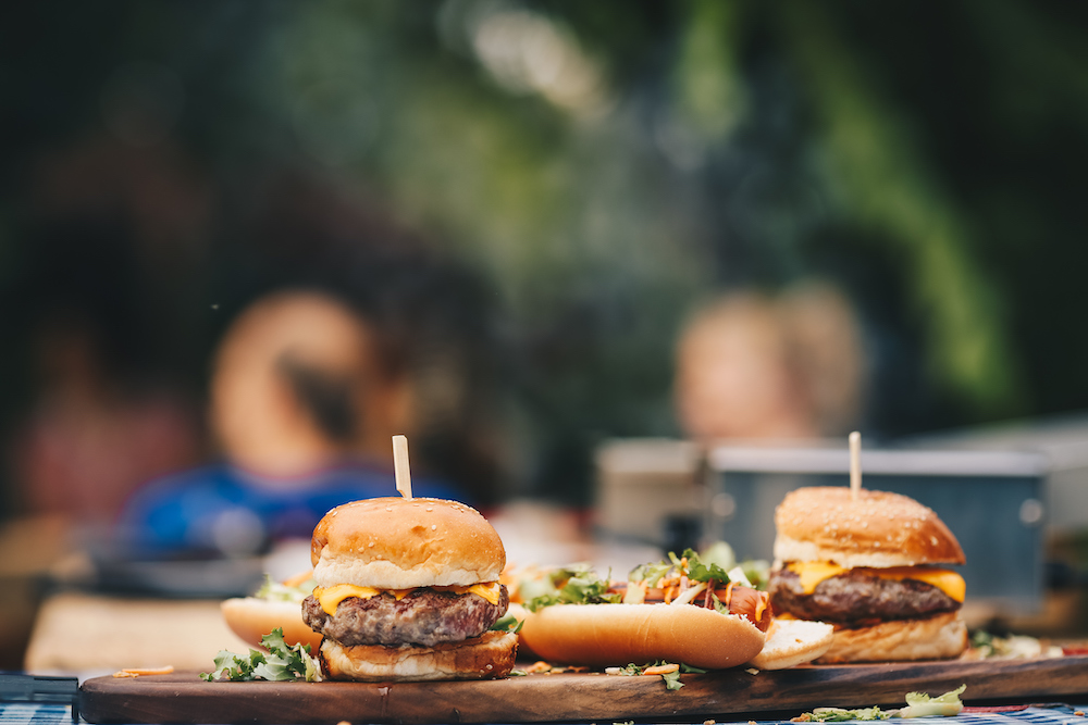Two burgers on a wooden serving platter at an outdoor table.