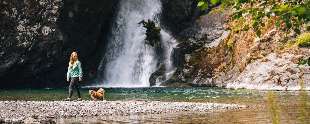 Young woman with dog explores waterfall in Washington state.