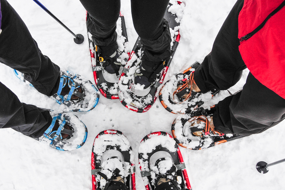 Four people standing on snow wearing modern, lightweight snowshoes