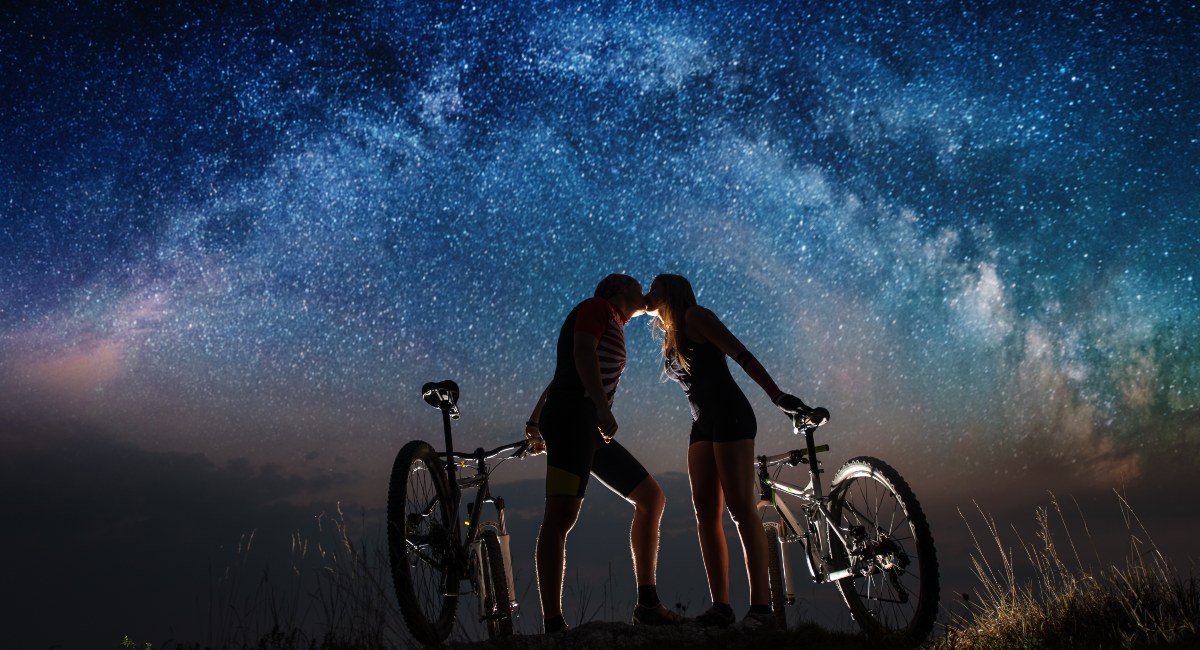 Couple with mountain bikes kissing under a clear night sky with stars