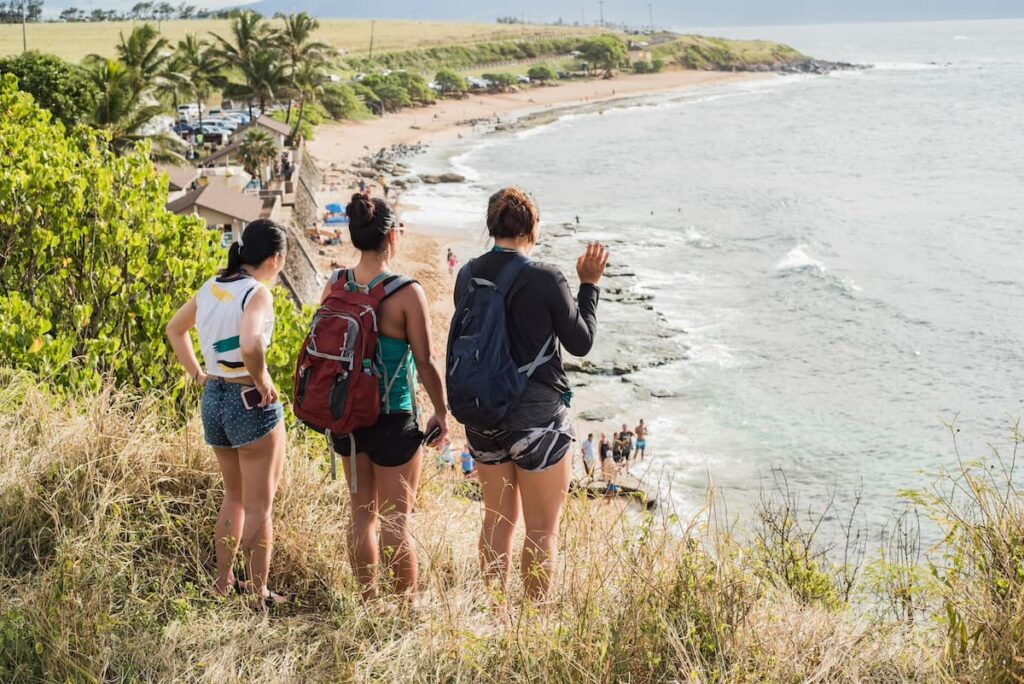 Three friends hiking a trail near a beach on Maui overlooking the ocean